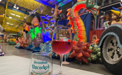 Wine glass and Shenandoah Uncorked event card with colorful sculptures in the background